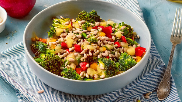 Ein Brokkolisalat in einer blauen Schüssel, dekoriert mit Sonnenblumenkernen und Paprika.