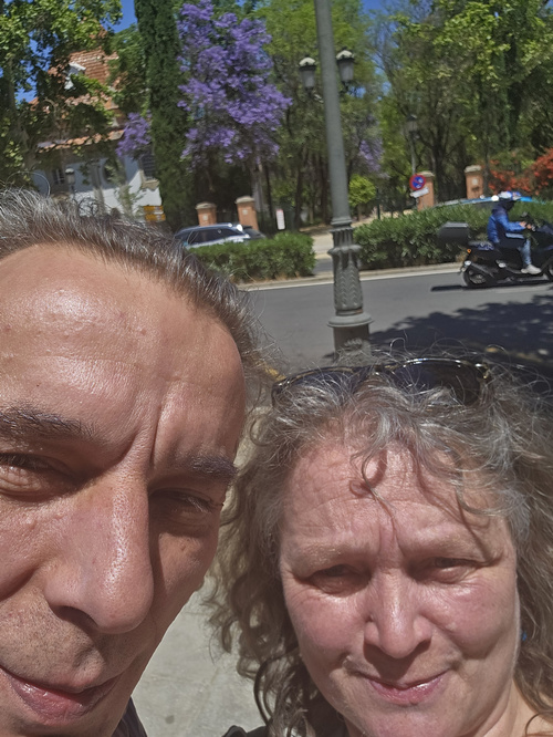 KI generiert: Zwei Personen machen ein Selfie im Freien; im Hintergrund sind Bäume und eine Straße.