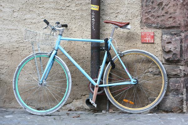 Hellblaues Herrenrad an Hauswand angelehnt 