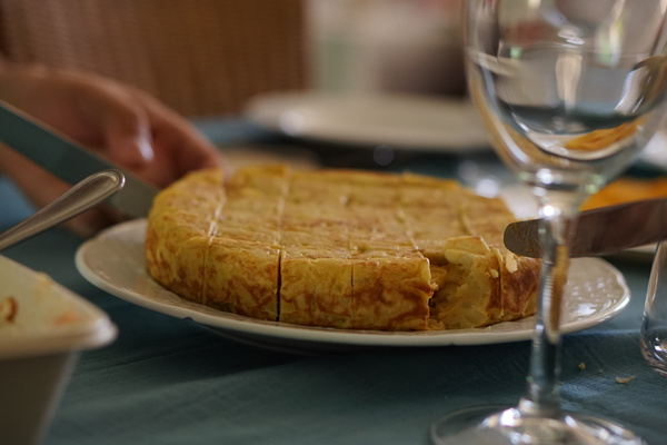 KI generiert: Eine angeschnittene Tortilla auf einem Teller mit Besteck und einem Weinglas auf einem gedeckten Tisch.