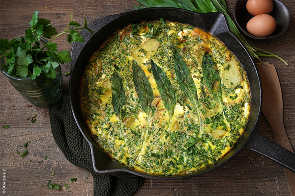 KI generiert: Eine Pfanne mit Kräuter-Frittata, dekoriert mit grünen Blättern. 