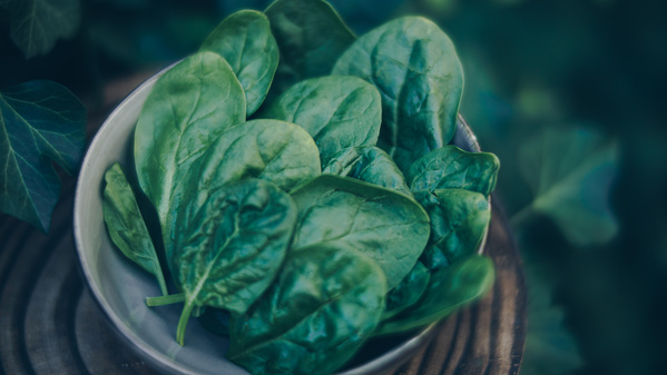 KI generiert: Schüssel mit frischem Spinat auf einem Holzuntergrund, im Hintergrund grüne Blätter.
