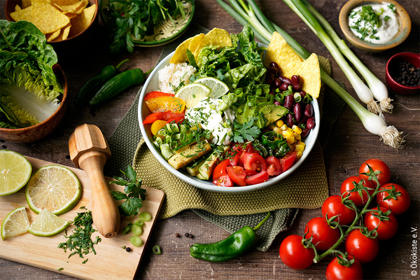 KI generiert: Bunter Salat in Schüssel mit Gemüse wie Tomaten, Mais, Avocado und Limetten. Frische Zutaten drumherum.
