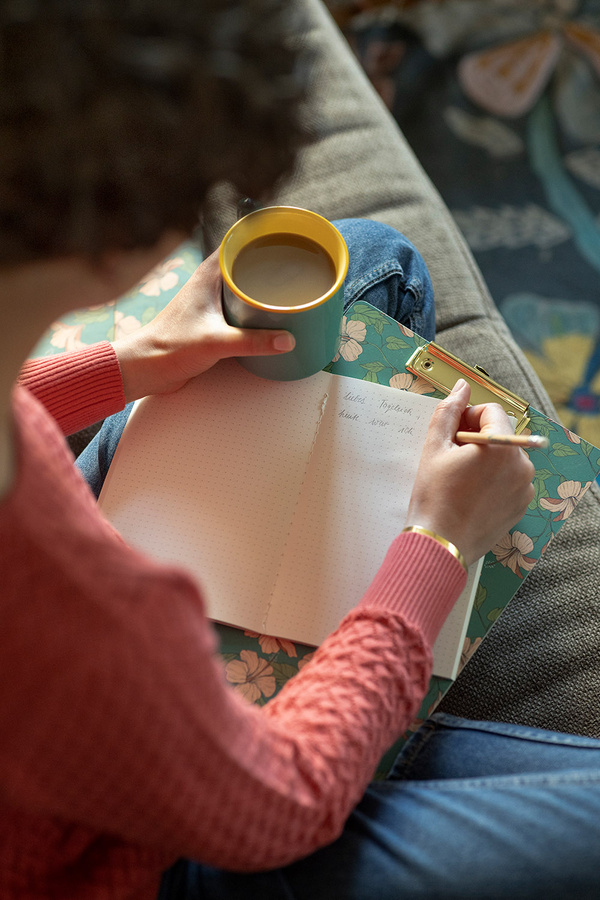 KI generiert: Person schreibt in Notizbuch, hält Tasse. Text: "Liebe Tagebuch, heute war ich".