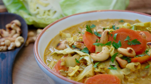 KI generiert: Ein Teller Curry mit Gemüse, Cashews und Kräutern, im Hintergrund ein Kohlkopf.