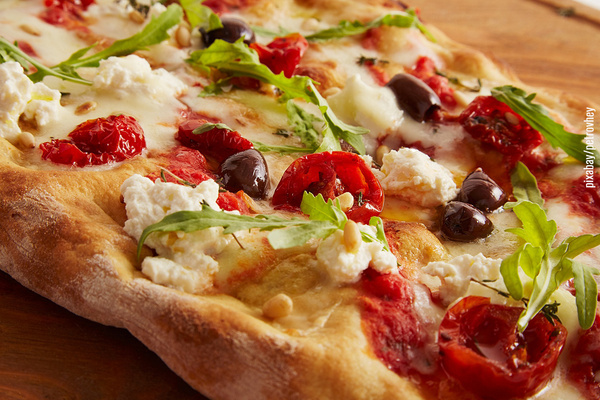 Pinsa belegt mit Tomaten, Oliven, Schafskäse und Rucola