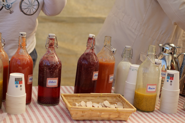 KI generiert: Hausgemachte Säfte in Glasflaschen mit Etiketten auf einem Tisch neben gestapelten Pappbechern.