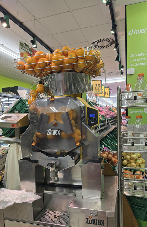 KI generiert: Eine Saftmaschine mit Orangen im Supermarkt. Text: "zümex".