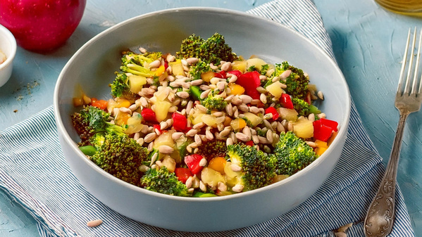 Schüssel mit Brokkoli-Salat, Paprika und Sonnenblumenkernen auf blauem Hintergrund.