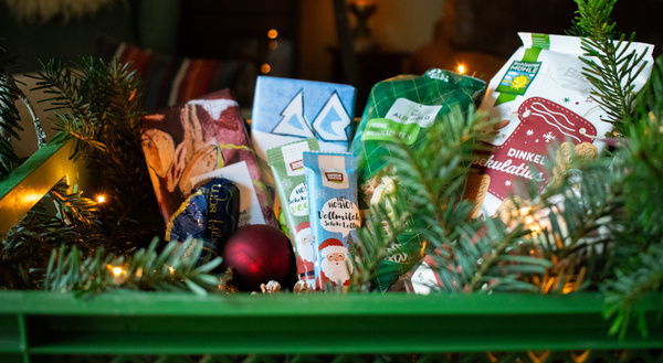 KI generiert: Eine grüne Kiste mit Weihnachtsprodukten, umgeben von Tannenzweigen und Lichtern.