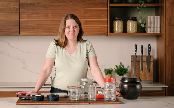 KI generiert: Eine Person steht in einer Küche hinter Gläsern und einem dunklen Behälter auf einer Arbeitsplatte.