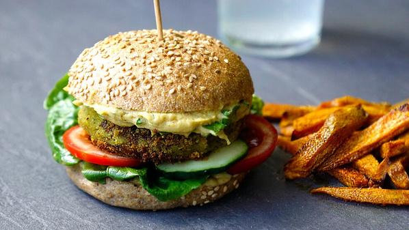 KI generiert: Ein vegetarischer Burger mit Salat, Tomate und Pommes auf grauem Hintergrund.