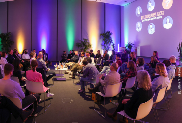 KI generiert: Leute sitzen im Kreis bei einer Veranstaltung, bunte Beleuchtung. Text: "Vollkorn Strikes Back?! Lifestyle & Planetary Health".