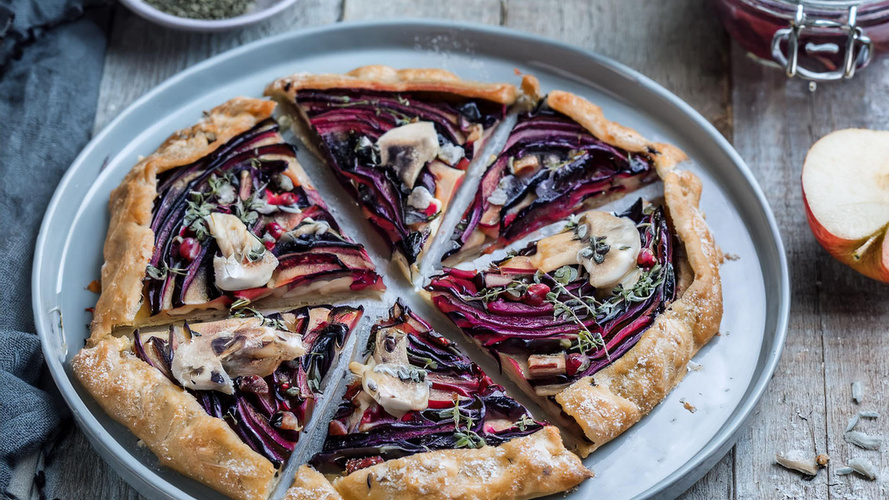 KI generiert: Eine rustikale Gemüsetarte mit lila und roten Zutaten auf einem Teller, in Stücke geschnitten.