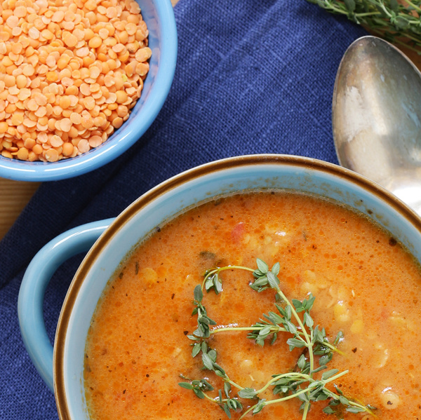 KI generiert: Blaue Schüssel mit roter Linsensuppe, garniert mit frischen Kräutern. Daneben rote Linsen in einer zweiten Schüssel.