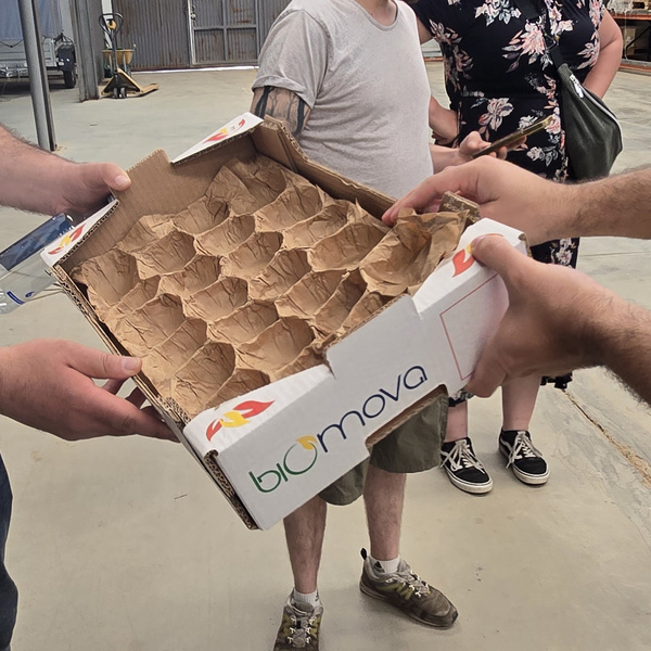 KI generiert: Leere Verpackungsschachtel von "biomova" aus Pappe wird von mehreren Personen gehalten.