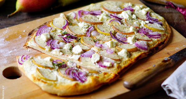 Flammkuchen mit roten Zwiebeln, Ziegenkäse und Birne angerichtet auf Holzbrett