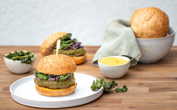 KI generiert: Ein vegetarischer Burger mit grüner Soße auf einem Teller, mit Beilagen wie Grünkohl und Senf auf einem Holztisch.
