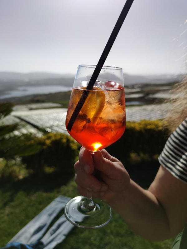 Aperol Spritz ins Sonnenlicht gehalten vor italienischer Hügellandschaft