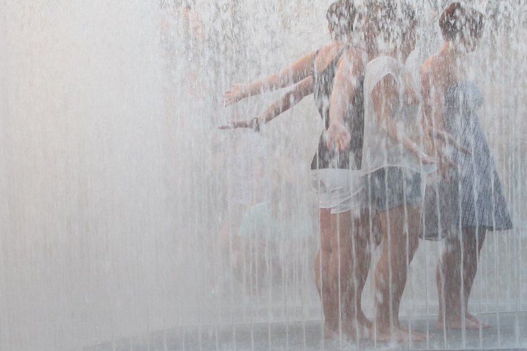 Gruppe von Frauen steht unter einem Springbrunnen und genießt die erfrischenden Spritzer.