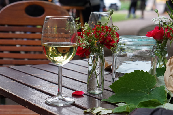 Weißweinglas auf Gartentisch mit Blumenväschen
