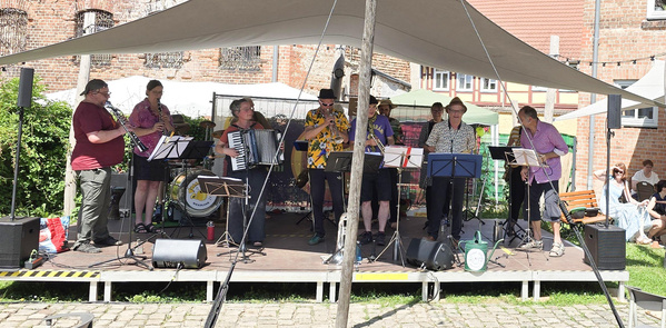 Eine Band spielt unter einem Zelt auf der Bühne mit Blas- und Akkordeoninstrumenten.
