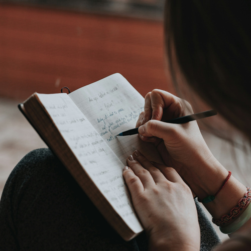 KI generiert: Eine Person schreibt in ein geöffnetes Notizbuch. Enthält handgeschriebenen Text.