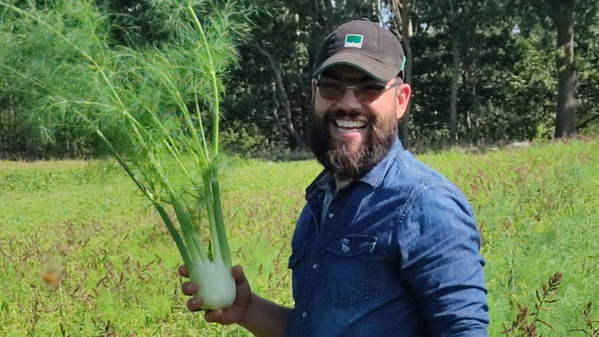Ein lächelnder Mann hält Fenchel auf einem Feld.