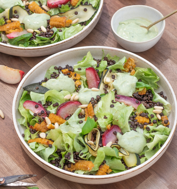 KI generiert: Ein bunter Salat mit Dressing, Linsen, Kürbis und Pinienkernen auf einem Holztisch.