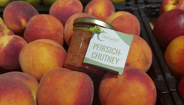 KI generiert: Ein Glas "Pfirsich-Chutney" von GrüViLand liegt auf frischen Pfirsichen.