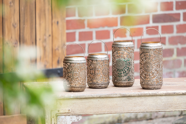 Metalllaternen mit filigranem Muster auf gartentisch vor Ziegelmauer