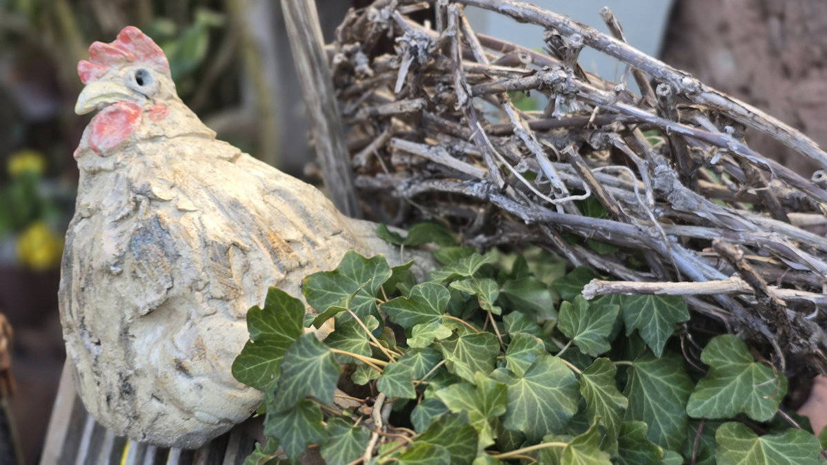 KI generiert: Tonfigur eines Huhns neben Efeublättern und Zweigen.
