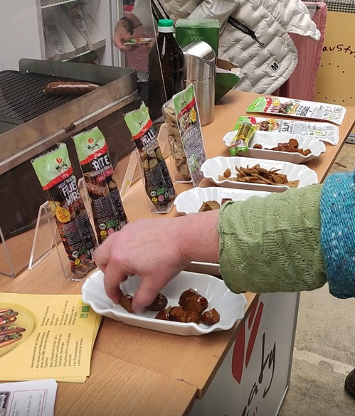 Wheaty hat mehrere vegane Würstchen angebraten und bittet Häppchen zum Probieren an