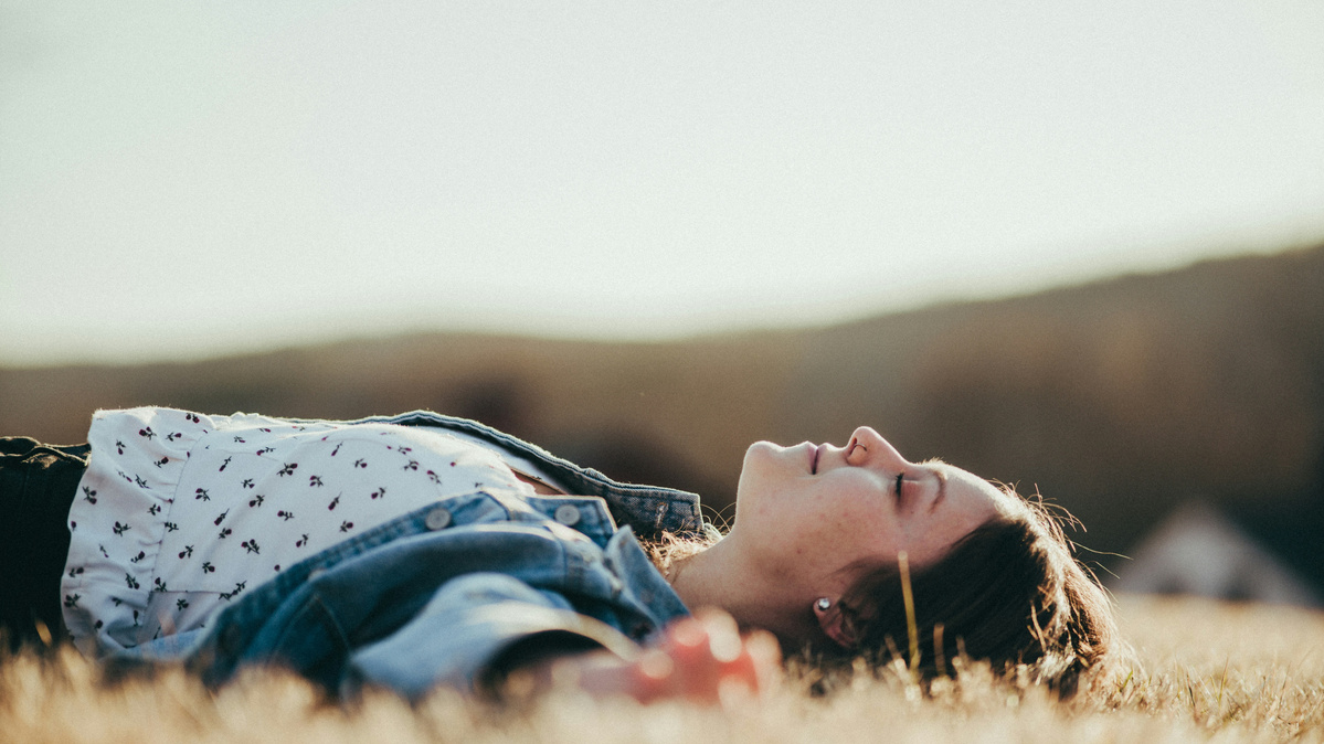 KI generiert: Eine Person liegt entspannt im Gras und genießt die Natur.