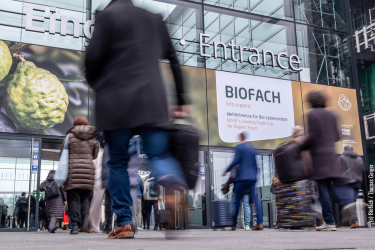 KI generiert: Menschen betreten eine Messehalle mit großem Schild: "BIOFACH: Weltleitmesse für Bio-Lebensmittel".