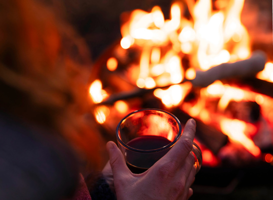KI generiert: Person hält eine Tasse am Lagerfeuer.