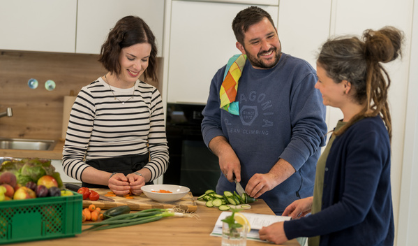 KI generiert: Drei Personen kochen und unterhalten sich in einer Küche.