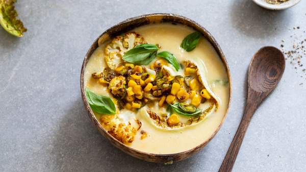 KI generiert: Eine Schüssel mit cremiger Suppe, Walnüssen, Mais und Basilikum dekoriert, daneben ein Holzlöffel.