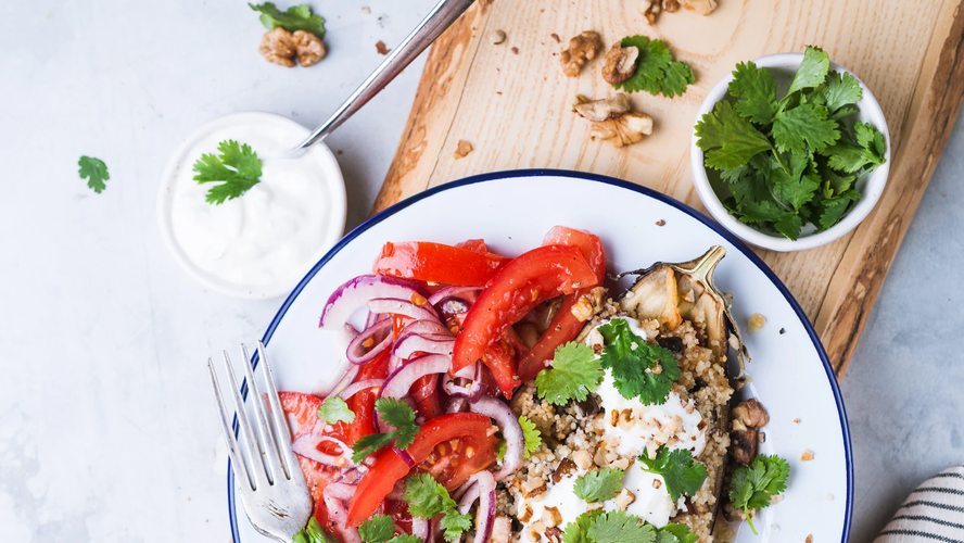 Weisser Porzellanteller mit blauem Rand, darauf eine gefüllte halbe Aubergine mit Tomatenachteln und roter Zwiebel
