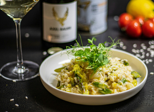 KI generiert: Ein Teller Risotto mit grünem Gemüse, daneben ein Glas Weißwein und eine Weinflasche im Hintergrund.