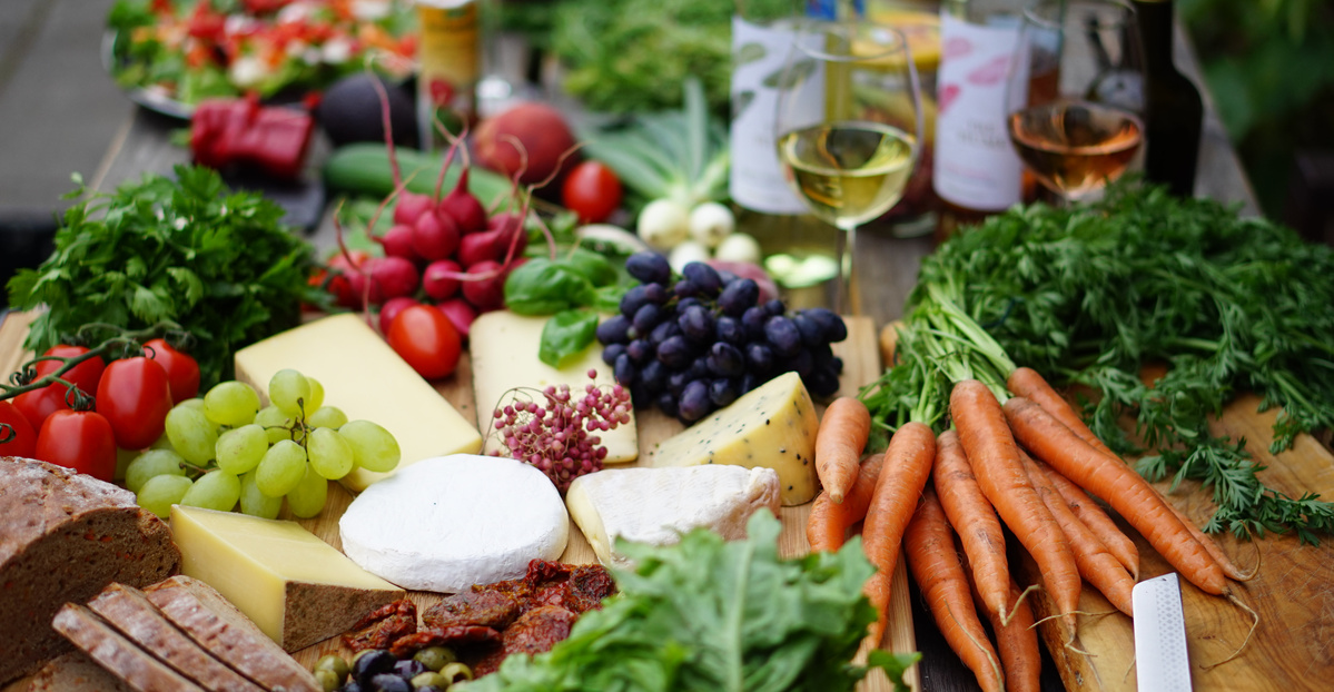 KI generiert: Eine Auswahl frischer Lebensmittel: Käse, Brot, Gemüse, Früchte und Wein auf einem Tisch.