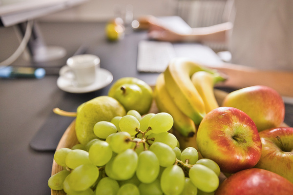 KI generiert: Ein Schreibtisch mit einer Schale voller Früchte: Trauben, Äpfel, Birnen und Bananen.