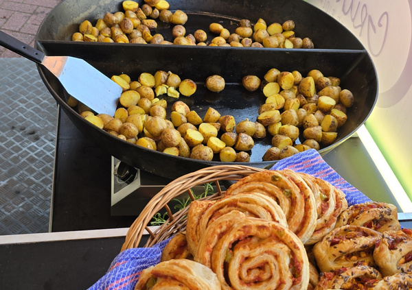 KI generiert: Bratkartoffeln in einer Pfanne und Gebäck in einem Korb auf einem Marktstand.