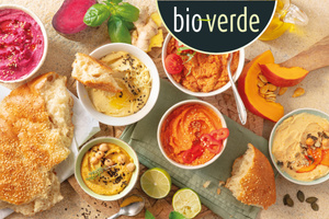 KI-generierte Beschreibung: Das Bild zeigt eine Auswahl an Bio-Lebensmitteln wie Brot, Nüsse, Gemüse und Aufstrichen. Text: "bioverde".