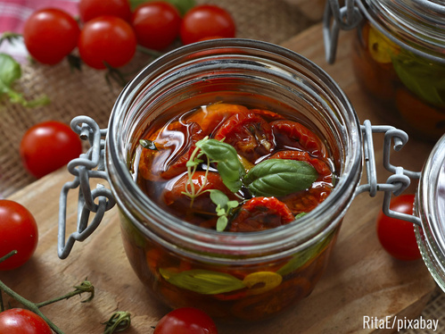 Geöffnetes Bügelglas mit in Öl eingelegten, getrockneten Tomaten und Basilikum