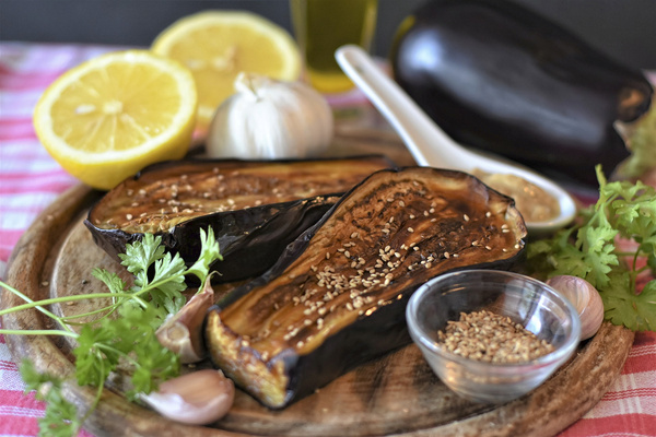 KI generiert: Geröstete Auberginen mit Sesam, Knoblauch, Zitronenhälften und Kräutern auf einem Holzbrett.