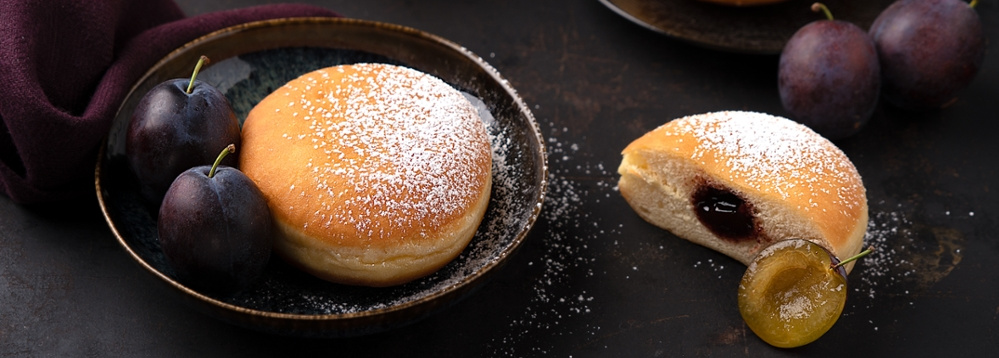 KI generiert: Ein Teller mit Pflaumen und einem Krapfen, der zur Hälfte aufgeschnitten ist.