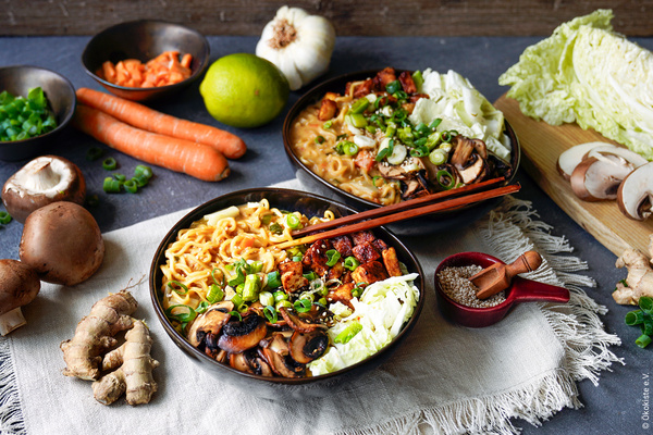 Thai-Ramen angerichtet in zwei Keramikschüsseln neben Zutaten