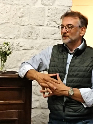 KI generiert: Ein Mann in Weste und Brille steht vor einer Steinwand, neben ihm ein Blumenstrauß auf einem Möbelstück.