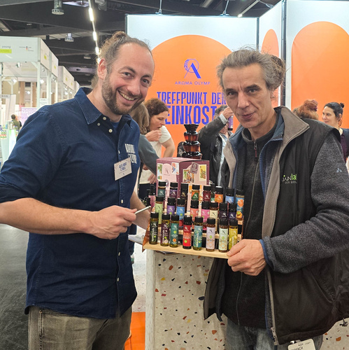 KI generiert: Zwei Männer präsentieren eine Auswahl bunter Produkte auf einem Tablett bei einer Messe. Text: "TREFFPUNKT DER FEINKOST".